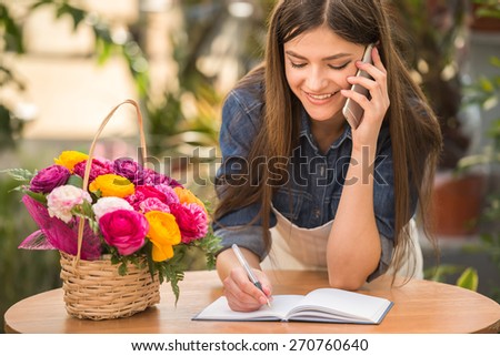 Portrait of young female florist talking on phone and making notes at flower shop.