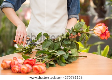 Close-up. Young female florist cutting a roses at flower shop.