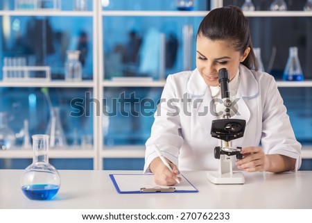 Attractive female scientist analysing something through a microscope and doing notes in a laboratory.