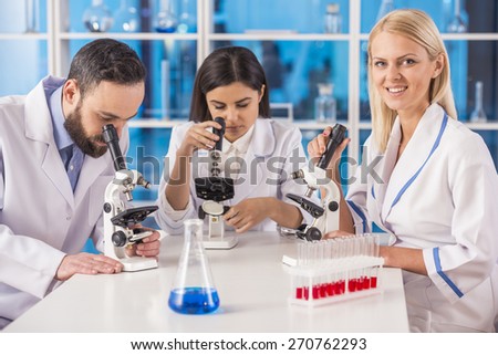 Science team working with microscopes in a laboratory. Female science looking at camera.