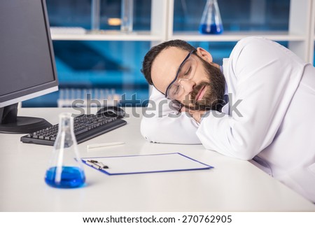 Handsome male scientist sleeping in safety glasses at his workplace in a laboratory.