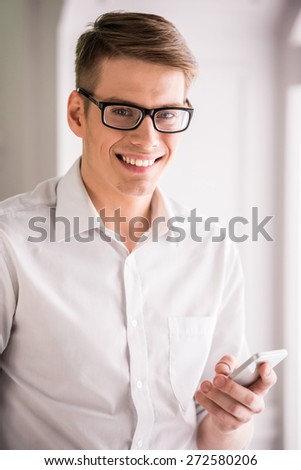 Handsome young man in glasses using phone and looking at camera.