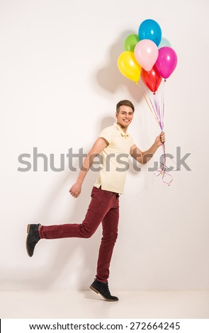 Young man with colorful balloons standing on grey background.