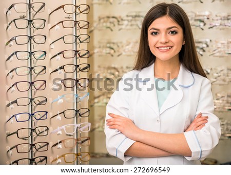 Optometrist is looking at the camera in glasses store. Professional young worker woman.