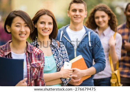 Group of young attractive smiling students dressed casual studying together in park.