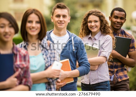 Group of young attractive smiling students dressed casual studying together in park.