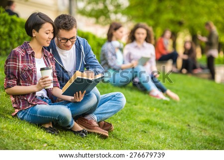 Couple of attractive smiling students dressed casual  studying outdoors on campus at the university.