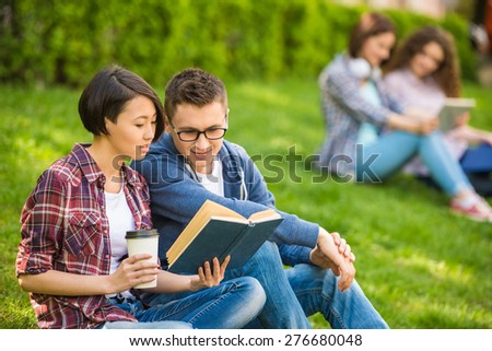 Couple of attractive smiling students dressed casual  studying outdoors on campus at the university.