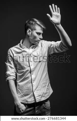 Young handsome man dressed casual showing open palm on dark background. Black and white fashion portrait.