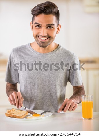 Young handsome man in grey t-shirt eating omelet and drinking juice for breakfast.