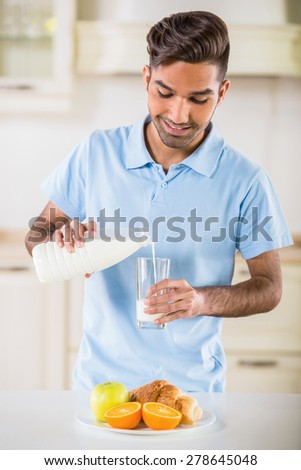 Young handsome man in blue t-shirt drinking milk and eating fruits for breakfast.
