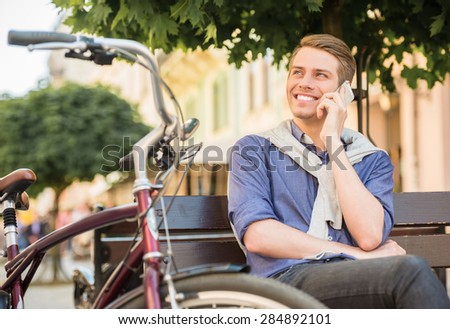 Young handsome man with bicycle sitting on the bench and resting.