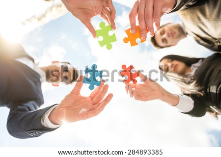 Closeup of business people wanting to put four pieces of puzzle together. Team work.