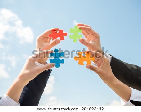 Closeup of business people wanting to put four pieces of puzzle together. Sky background.