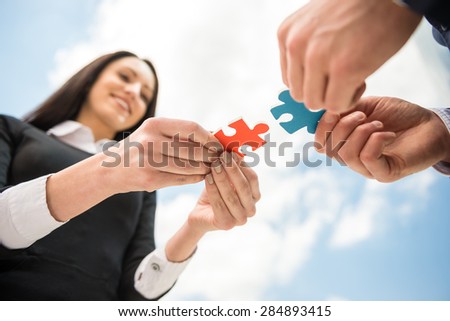 Closeup of business people wanting to put two pieces of puzzle together. Sky background.