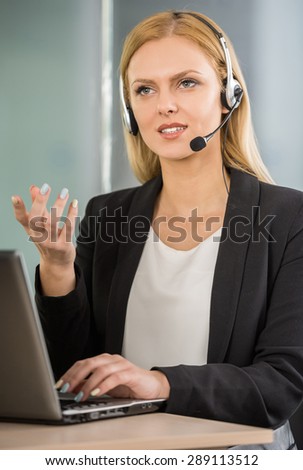 Beautiful young woman with headset sitting at office and using laptop.