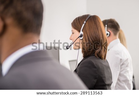 Call centre workers working in line with their headsets. Back view.
