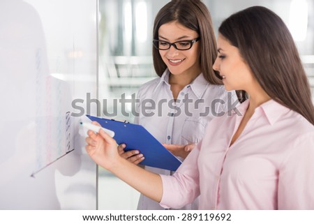 Two beautiful office workers drawing business strategy on flip chart.