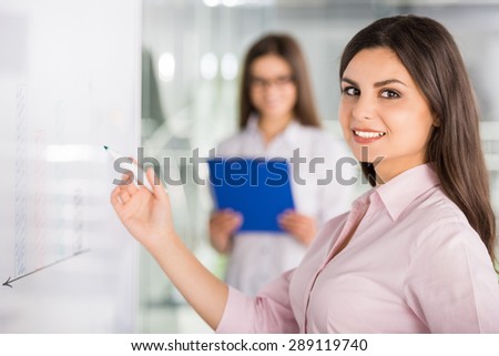 Two beautiful office workers drawing business strategy on flip chart.