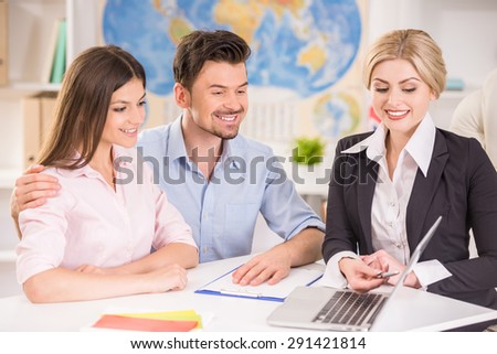 Attractive travel agent showing catalog with tours to happy young couple.