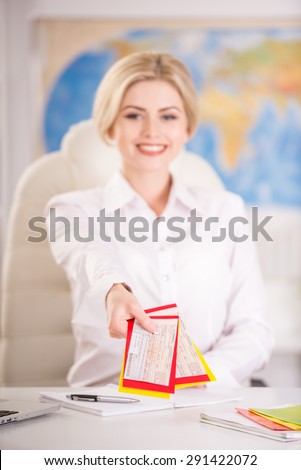 Female travel agent sitting at office and holding tickets.