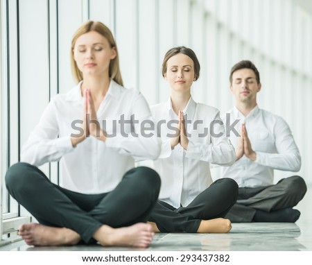 Business team doing yoga exercise in office together, sitting on the floor with closed eyes.
