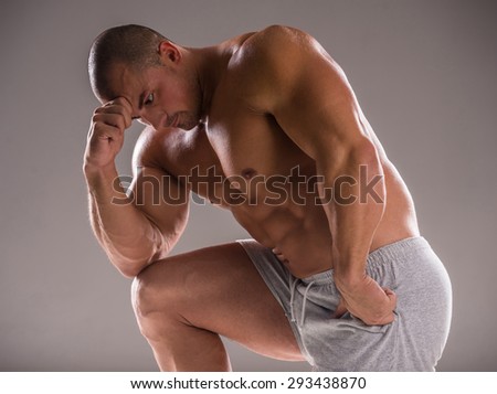 Bodybuilder in good shape against gray background. Man posing, showing his muscle definition.