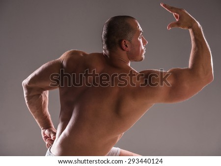 Beautiful muscular man bodybuilder posing back over dark background.