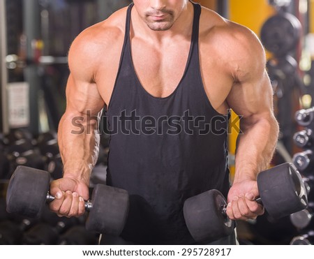 Muscular bodybuilder guy doing exercises with dumbbells at gym, close-up.