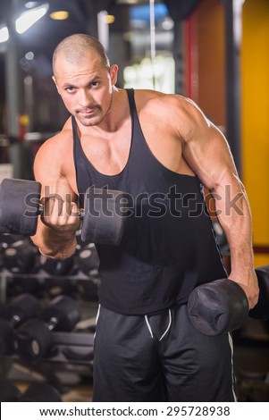 Handsome power athletic man in training pumping up muscles with dumbbell.