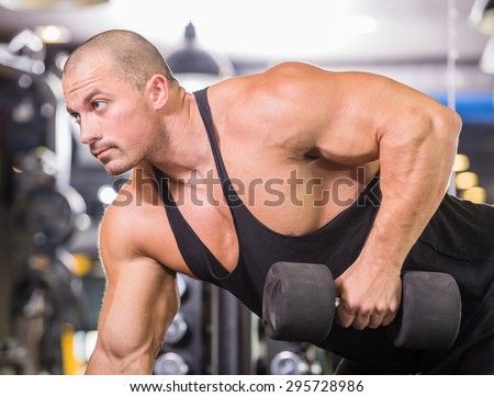 Muscular male bodybuilder working out in gym, exercising triceps leaning on a bench.