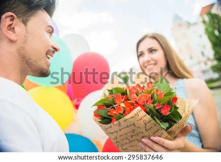 Romantic date outdoors. Handsome man surprised his woman with flowers and colorful balloons. Focus on flowers.