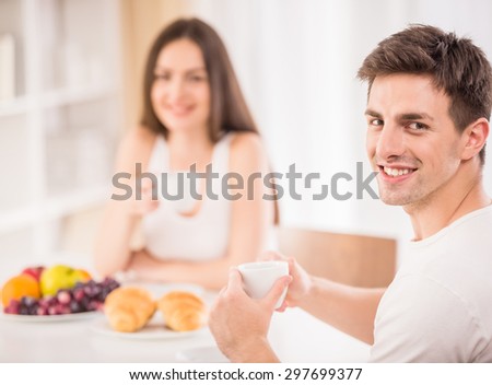 Young family couple sitting at the table in the kitchen and having breakfast together.