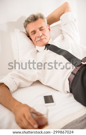 Businessman sleeping on bed after hard working day with glass of whiskey and his phone at the hotel room.