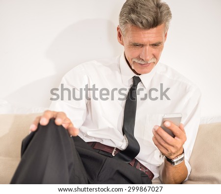 Businessman holding his phone and looking at it while sitting on bed at the hotel room.