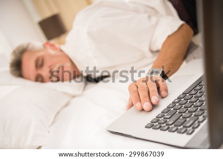 Businessman sleeping on bed after hard working day with his laptop at the hotel room. Side view.