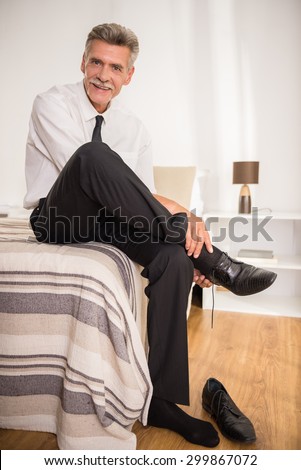 Mature man dressed formal going to bed after hard working day at the hotel room and looking at camera.