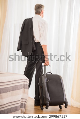 Businessman with his suitcase at the hotel room looking at the window. Back view.