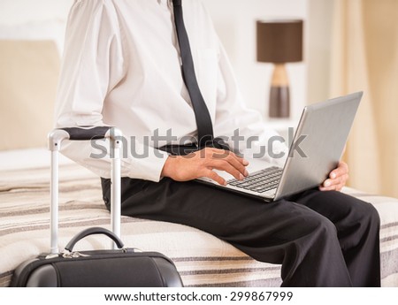 Businessman using laptop while sitting on bed at the hotel room. Close-up.