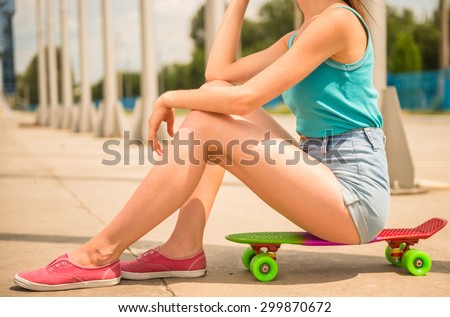 Young woman sitting on skateboard at the city street. Close-up.