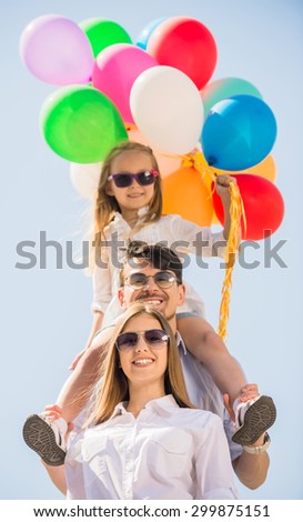 Happy family holding colorful balloons outdoor. Mom, dad and little daughter playing together.