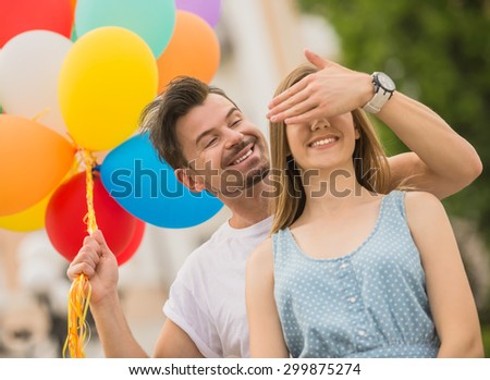 Handsome man surprising his girlfriend with colorful balloons. Romantic date outdoors.