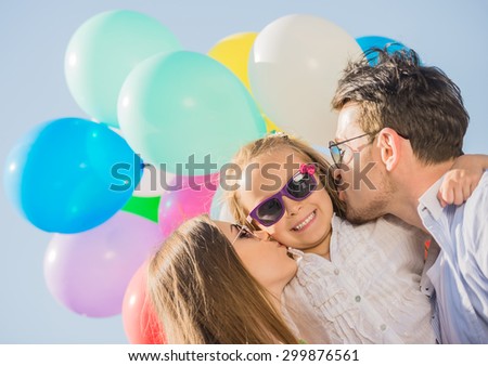 Young attractive parents with balloons kissing their little daughter on the cheek.