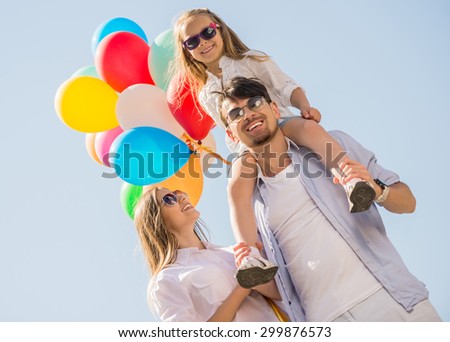 Young smiling family with colorful balloons walking on sunny day. Front view.