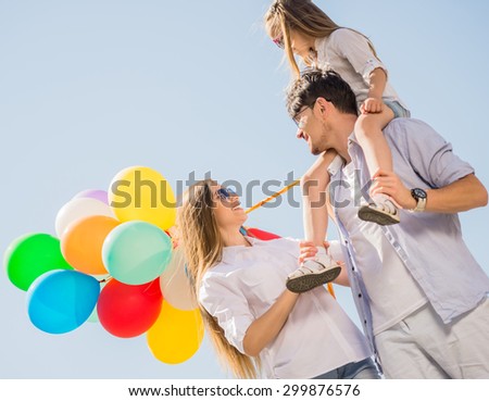 Young smiling family with colorful balloons walking on sunny day.