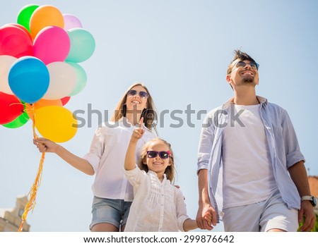 Happy family with balloons looking up outdoor on a summer day, daughter pointing at the top.