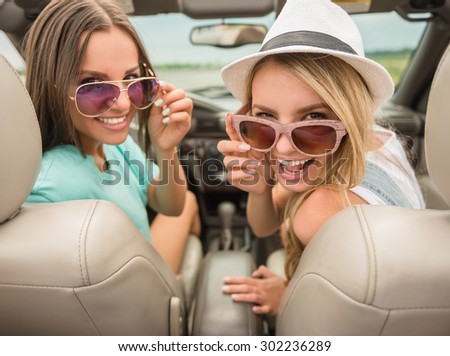 Cheerful young woman in cabriolet looking back at camera and smiling.