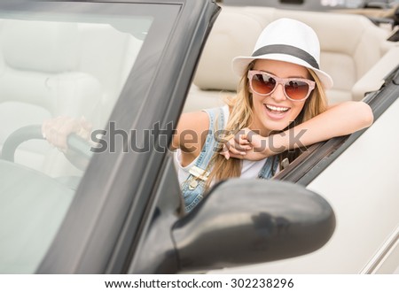 Attractive woman sitting in cabriolet, looking at camera and smiling.