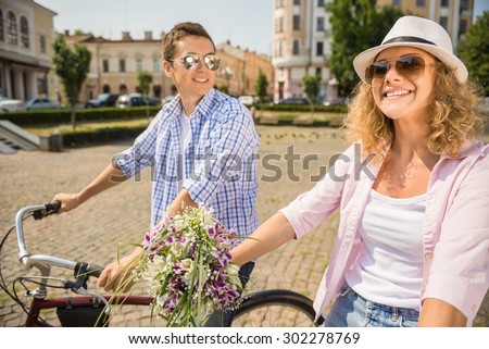 Cheerful couple in sunglasses riding on bicycles on the city street. Man looking at her girlfriend.