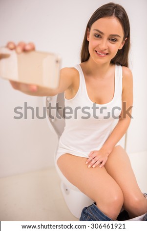 Pretty girl on toilet with cell phone and smiling. Woman sitting with mobile in toilet on white
